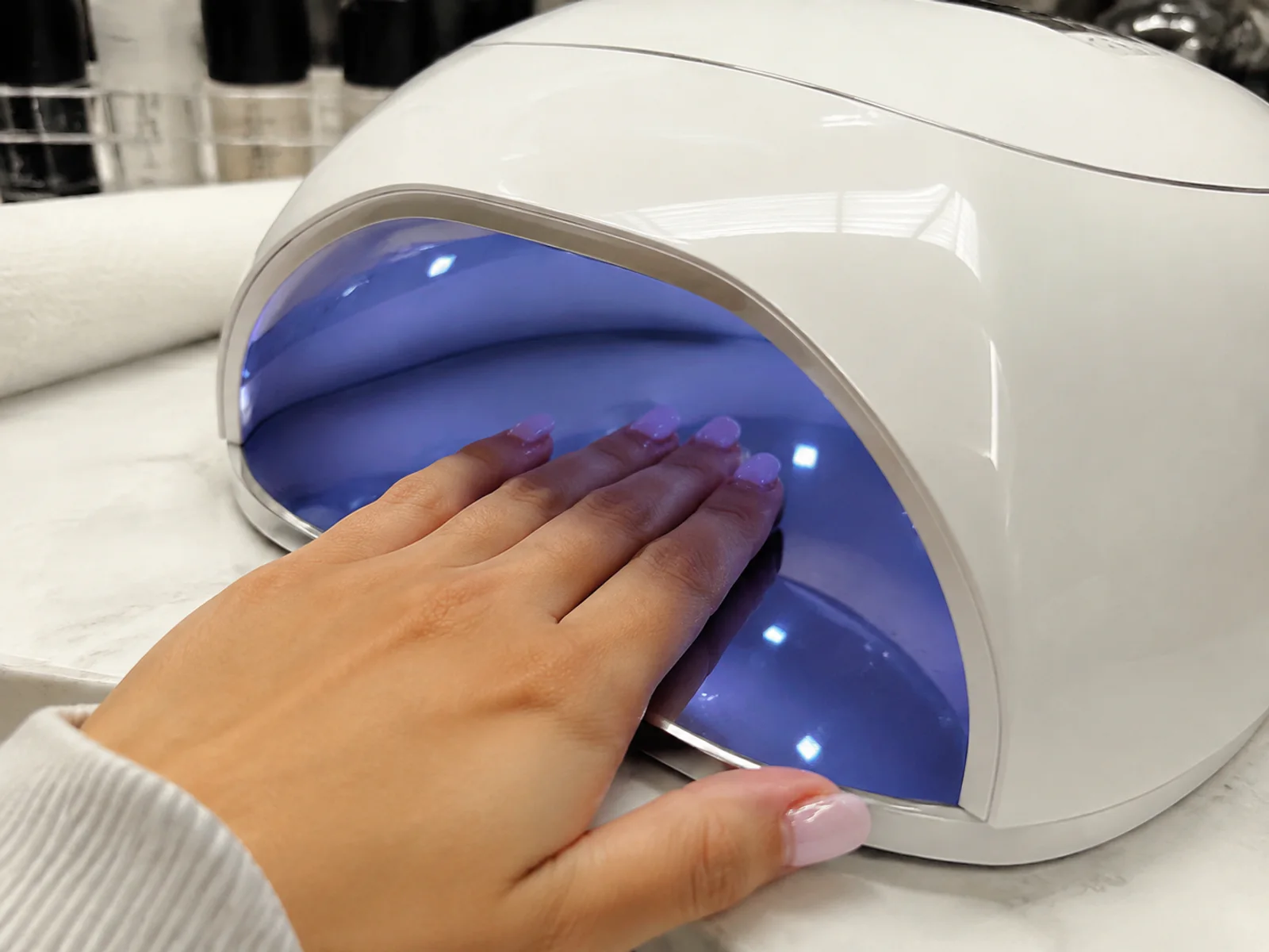 Les doigts manucurés de la cliente correctement positionnés à l'intérieur d'une lampe à ongles professionnelle UV/LED.