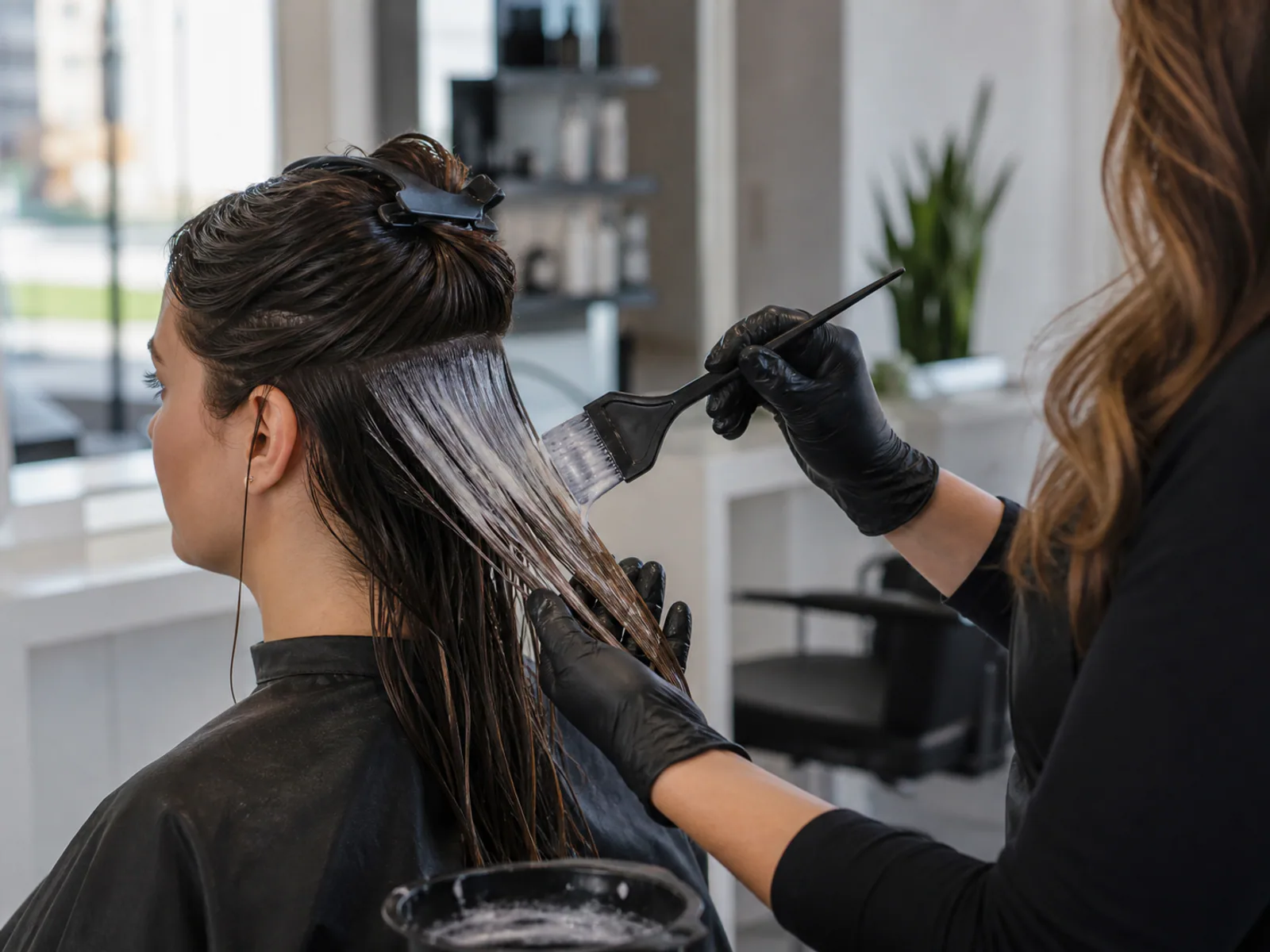 Un styliste professionnel appliquant un traitement de correction de couleur par bain décolorant sur les cheveux d'un client dans un salon.