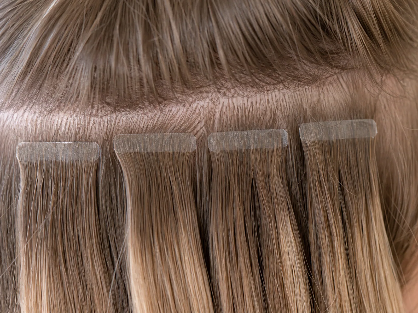 Close up view of professional tape-in hair extension adhesive bonds applied near the scalp.